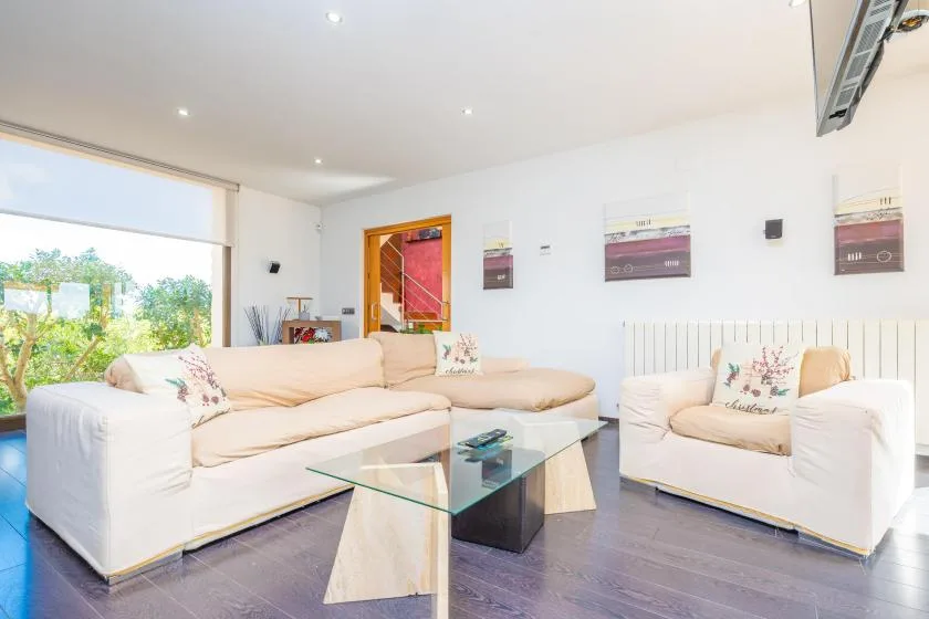 A bright living room with light-colored seating and a glass coffee table.