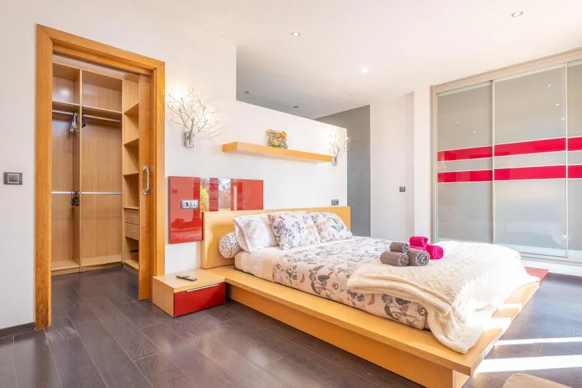 A bedroom with a low bed and an open wooden wardrobe.