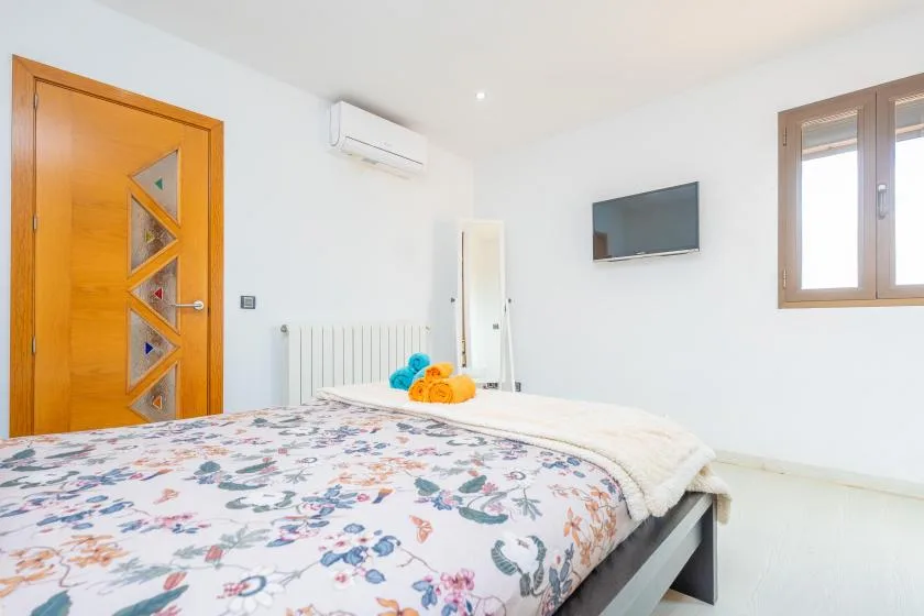 A bright bedroom with a floral bedspread and a wall-mounted television.