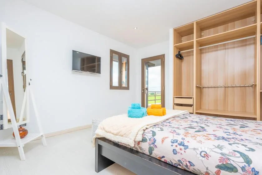 A bedroom with a floral bedspread and an open wooden wardrobe.