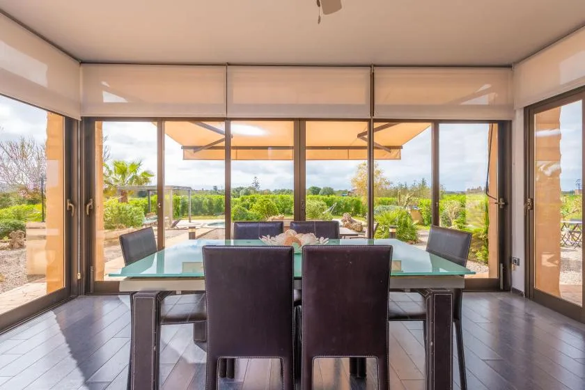 A dining area with a glass table and seating, opening onto a garden.