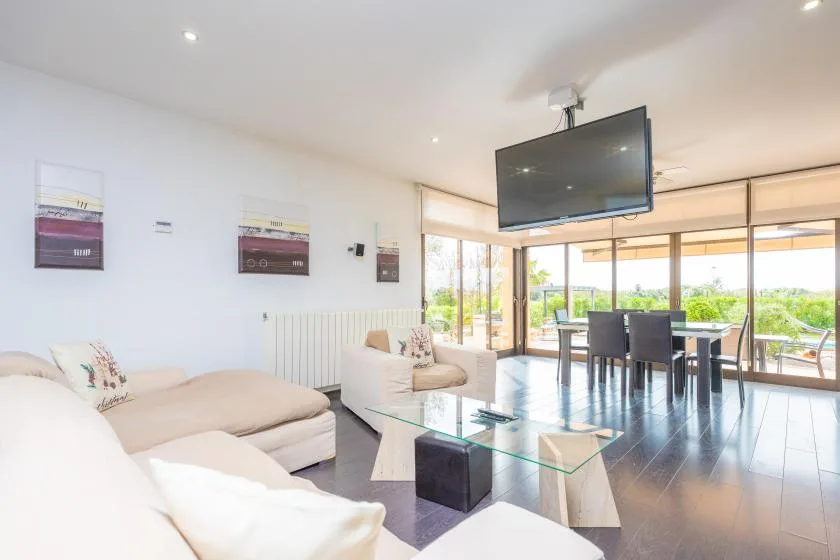 A bright living room with seating, a glass coffee table, and large windows.