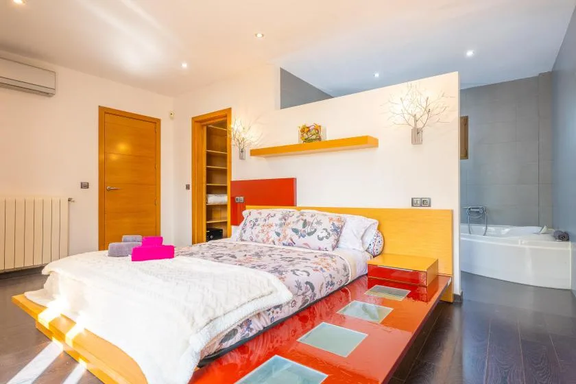 A bedroom with a bed and a bathtub visible in the adjoining bathroom.