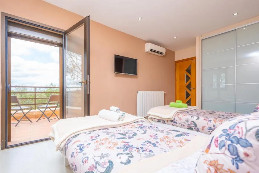 A bedroom with floral bedding, an open balcony door, and a wall-mounted television.
