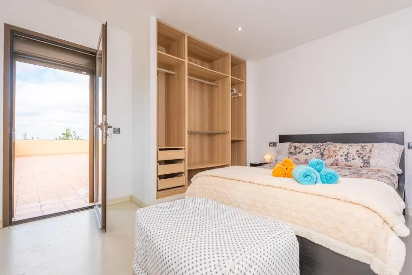 A bright bedroom with a bed and an open wardrobe beside a glass door.