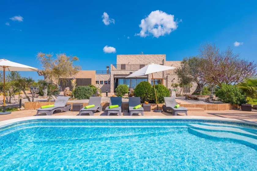 A swimming pool with seating and umbrellas in front of a modern building.