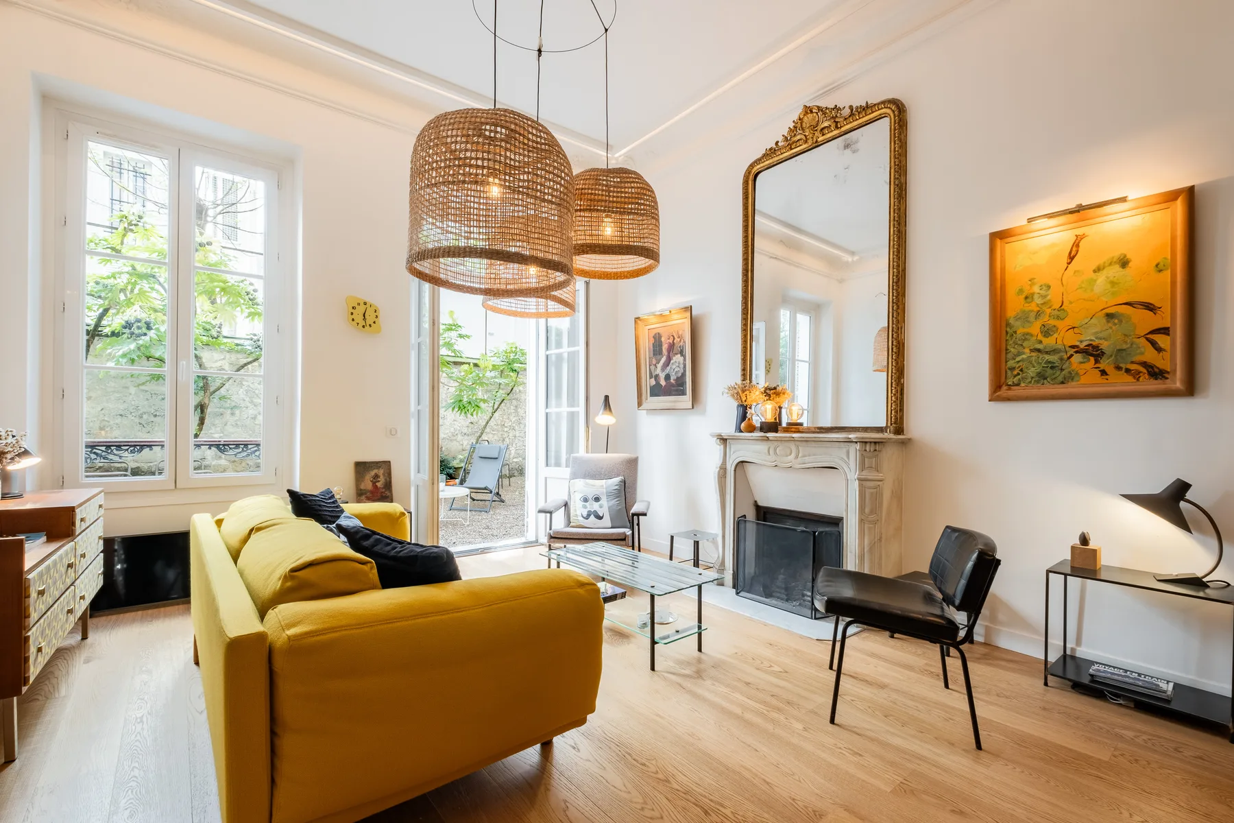A bright living room with yellow seating, tall windows, and a fireplace.