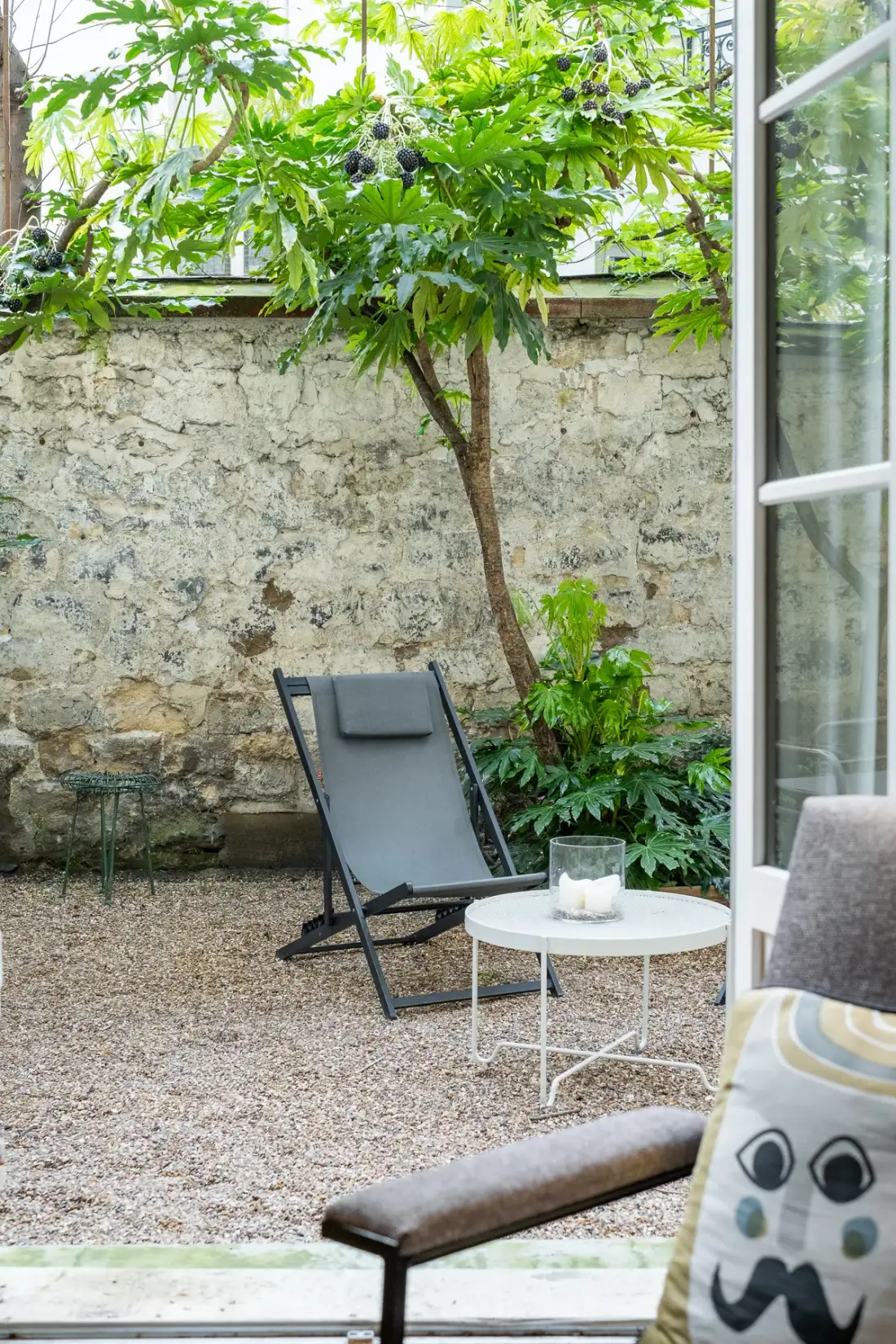 A small garden seating area with a tree, gravel ground, and a round table.