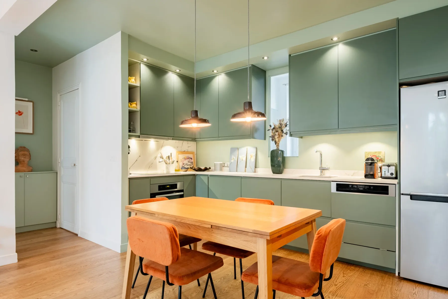 A modern kitchen with green cabinets and a wooden dining table.