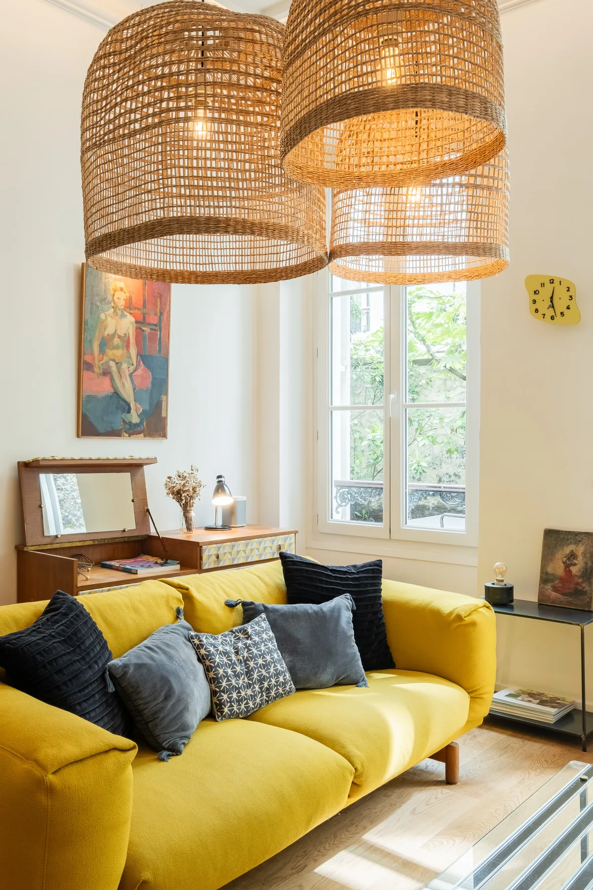 A bright living room with a yellow sofa beneath woven pendant lights.
