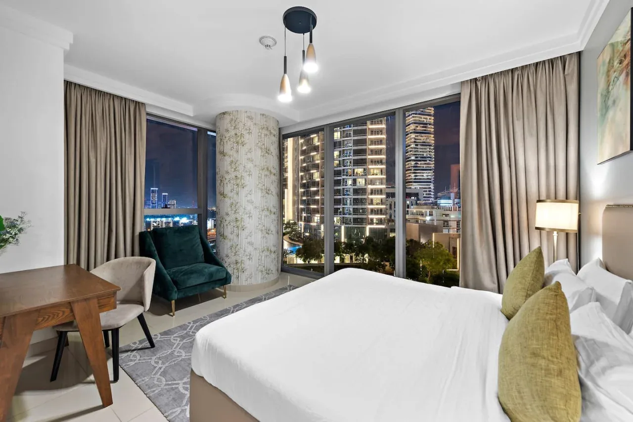 Un dormitorio con una cama grande, asientos y ventanales con vistas a las luces de la ciudad.