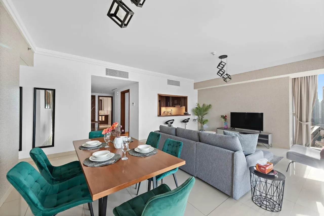 Una moderna sala y comedor con asientos verde azulado y un televisor.