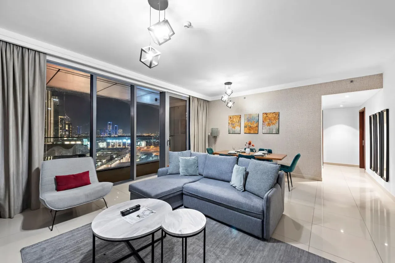 Una sala de estar con asientos junto a ventanales con vistas a una ciudad de noche.