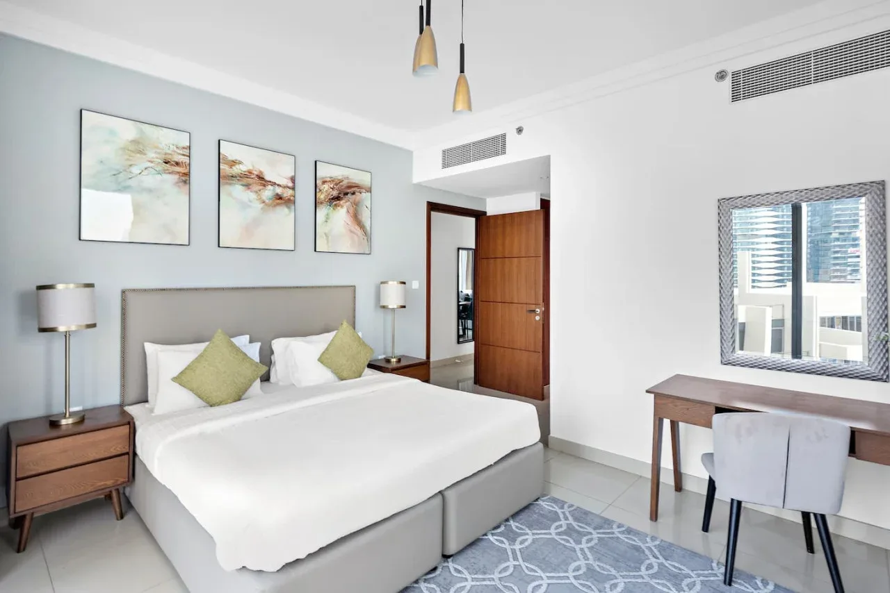 Un dormitorio luminoso con una cama bien tendida y un escritorio junto a la ventana.