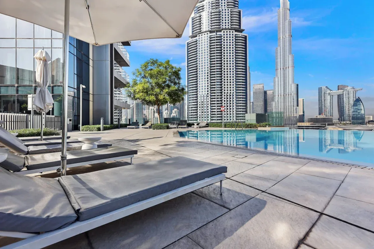 Una terraza con piscina, asientos de descanso y el perfil urbano al fondo.