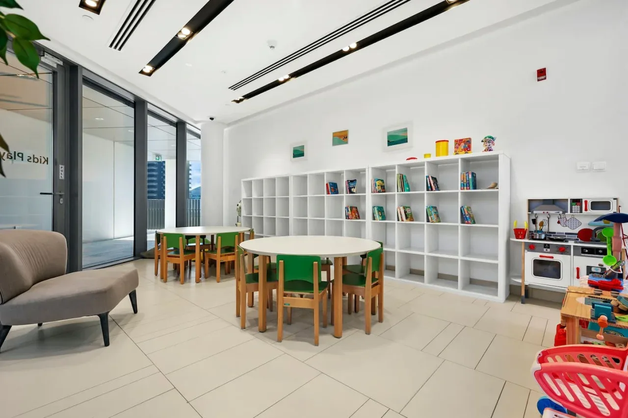 Una luminosa sala de juegos infantil con mesas, asientos, estantes y juguetes.
