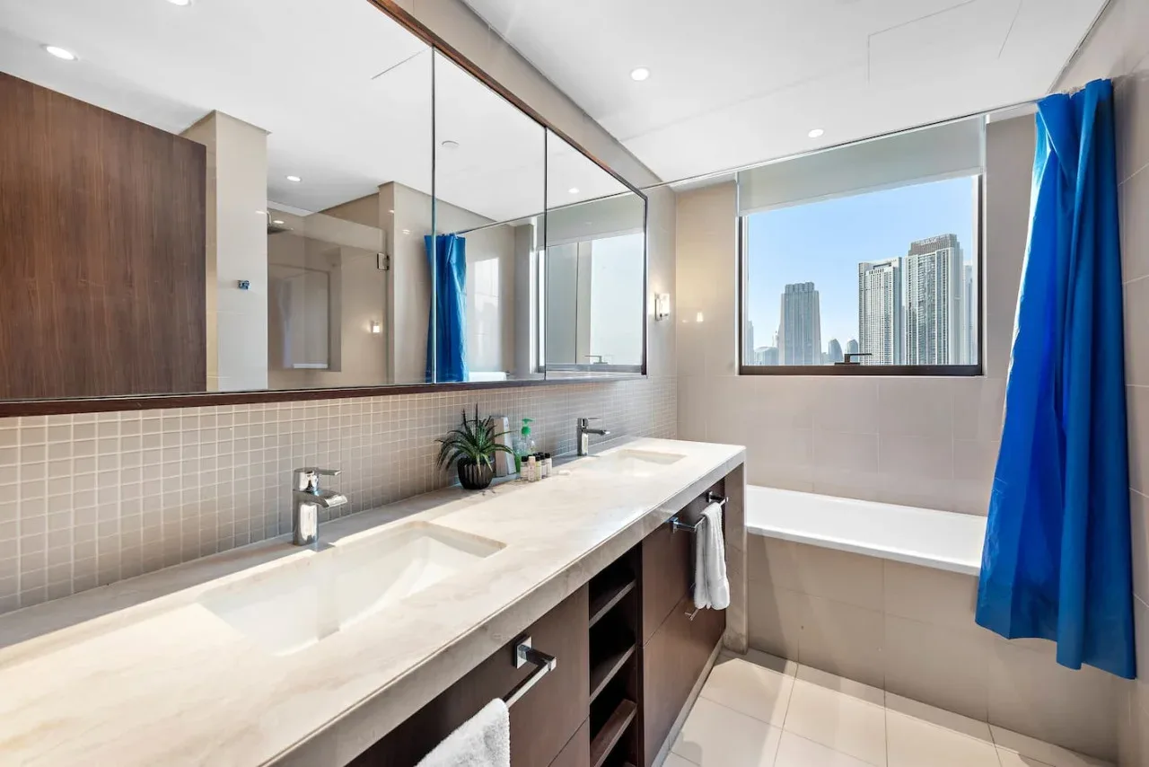 Un baño luminoso con un mueble largo, dos lavabos y una bañera.