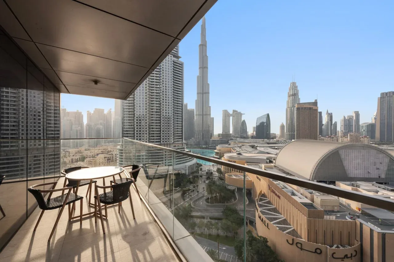 Una zona de comedor en un balcón da a un horizonte urbano con una torre destacada.