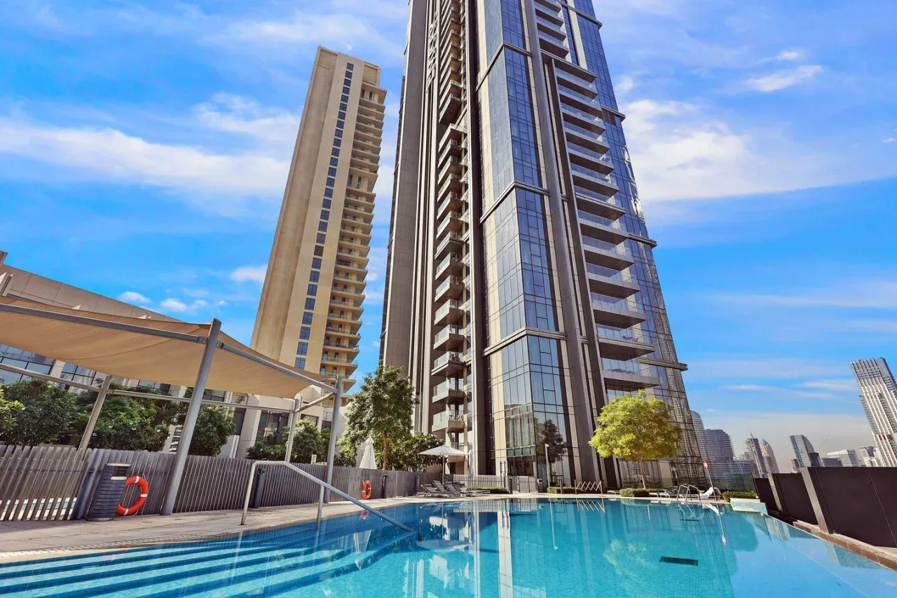 Una piscina está junto a altos edificios residenciales modernos bajo un cielo azul.