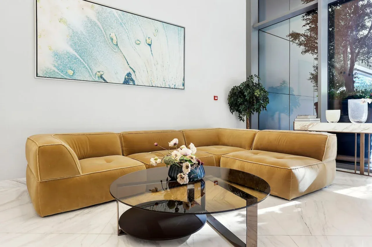 Una sala luminosa con un sofá seccional color tostado y una mesa de centro de vidrio.