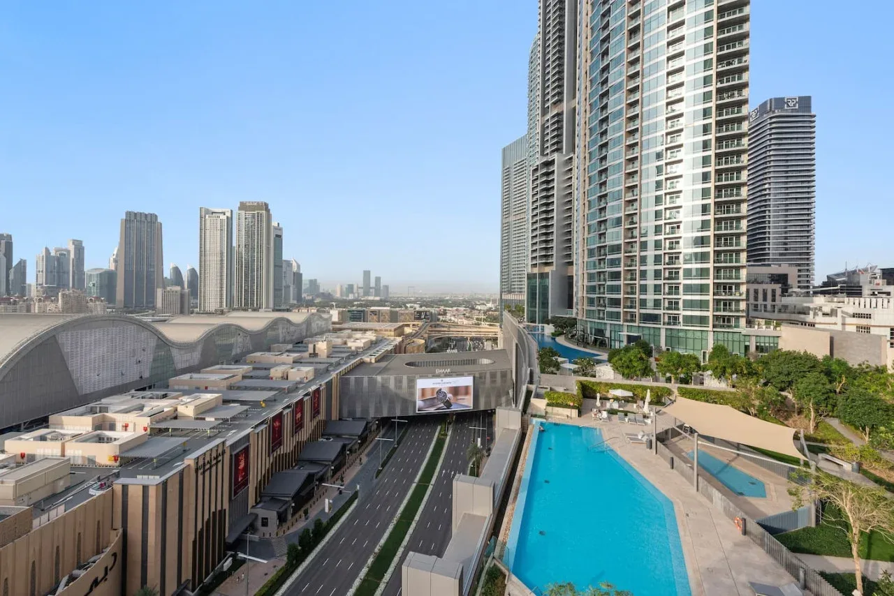 Una vista urbana de edificios altos domina una larga piscina al aire libre y las construcciones cercanas.