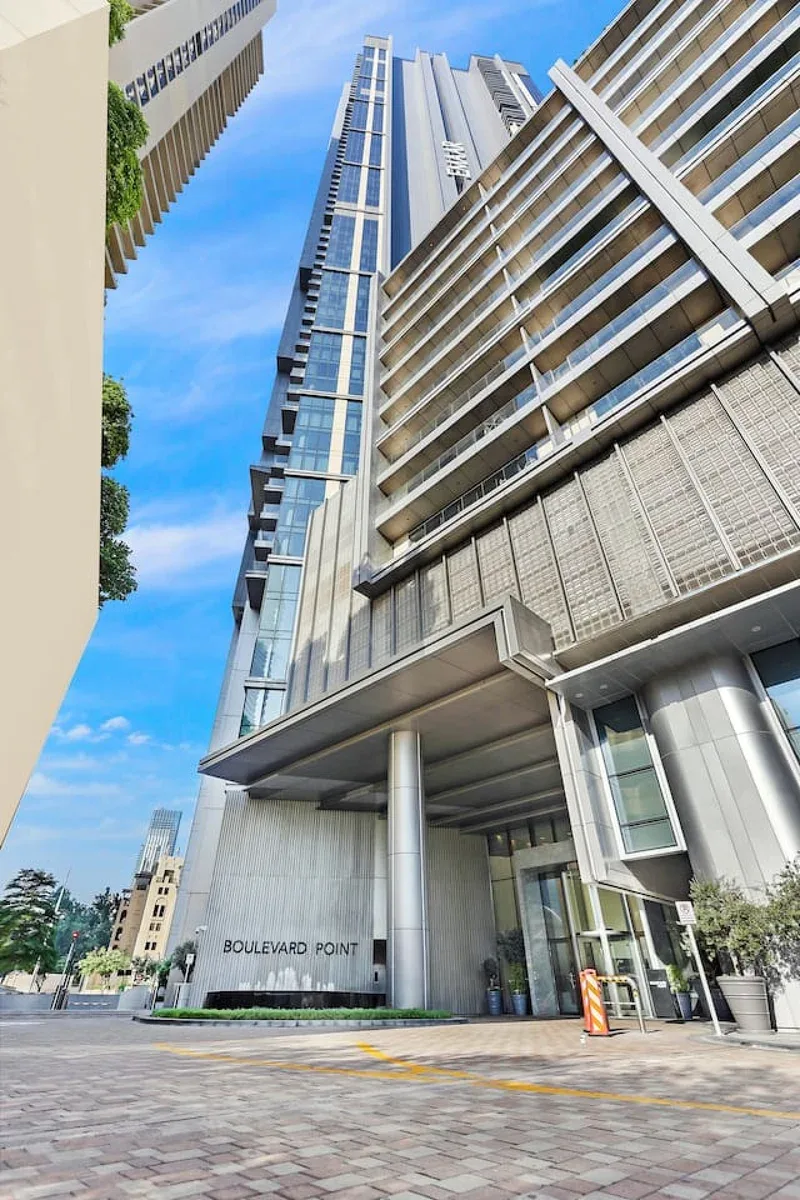 Un edificio moderno de gran altura se eleva sobre una plaza de entrada pavimentada.