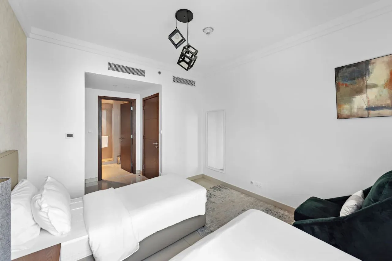Un dormitorio luminoso con ropa de cama blanca, una zona de asientos oscura y un cuadro abstracto.