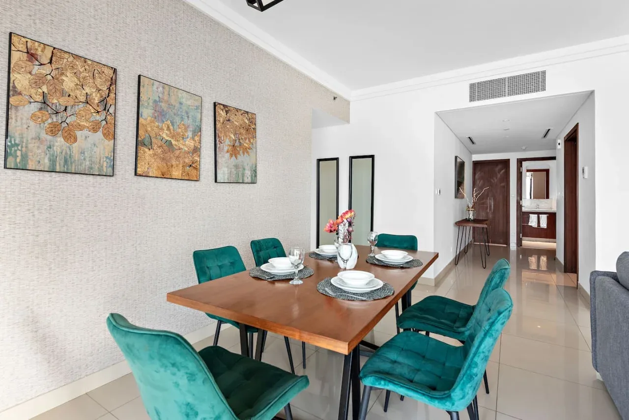 Comedor con una mesa de madera, asientos turquesa y cuadros florales.