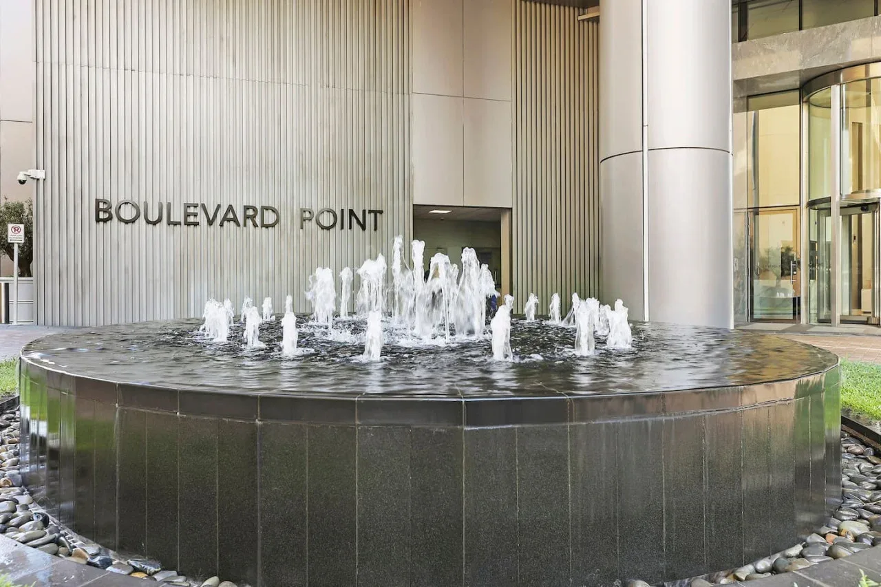 Una fuente circular con chorros de agua está frente a la entrada de un edificio moderno.