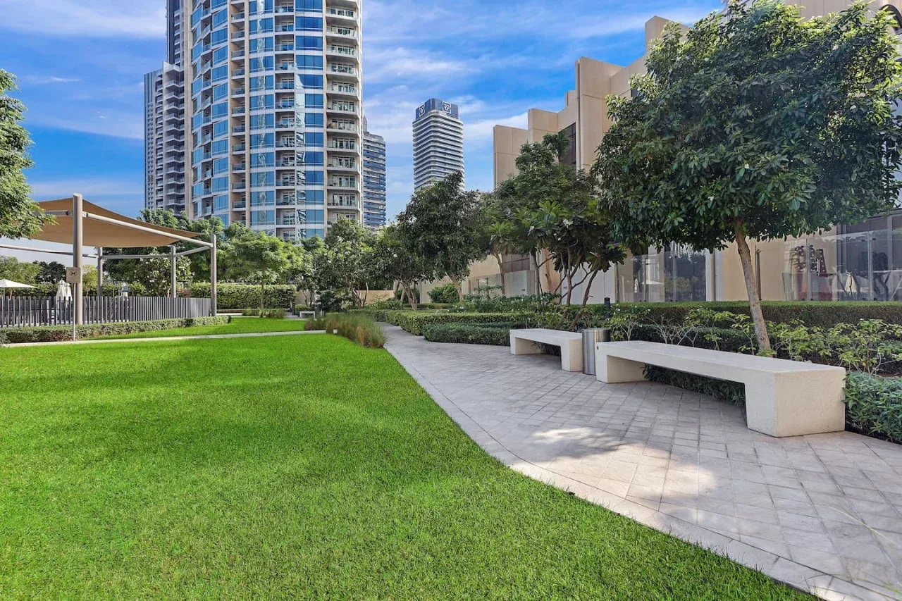Un patio ajardinado con un sendero pavimentado, césped verde y árboles.
