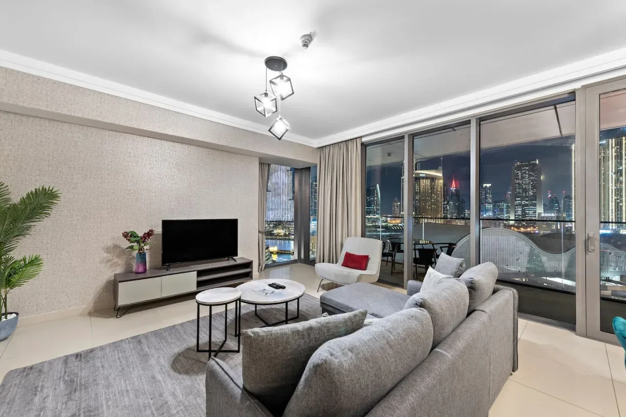 A living room with seating and large windows overlooking a city skyline at night.