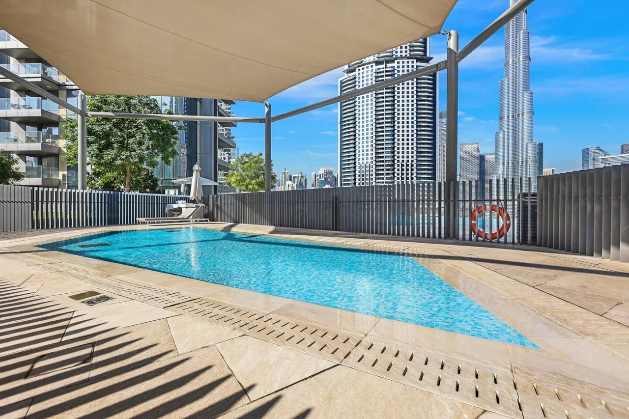 Una piscina al aire libre junto a un perfil urbano de rascacielos, bajo una cubierta de sombra.