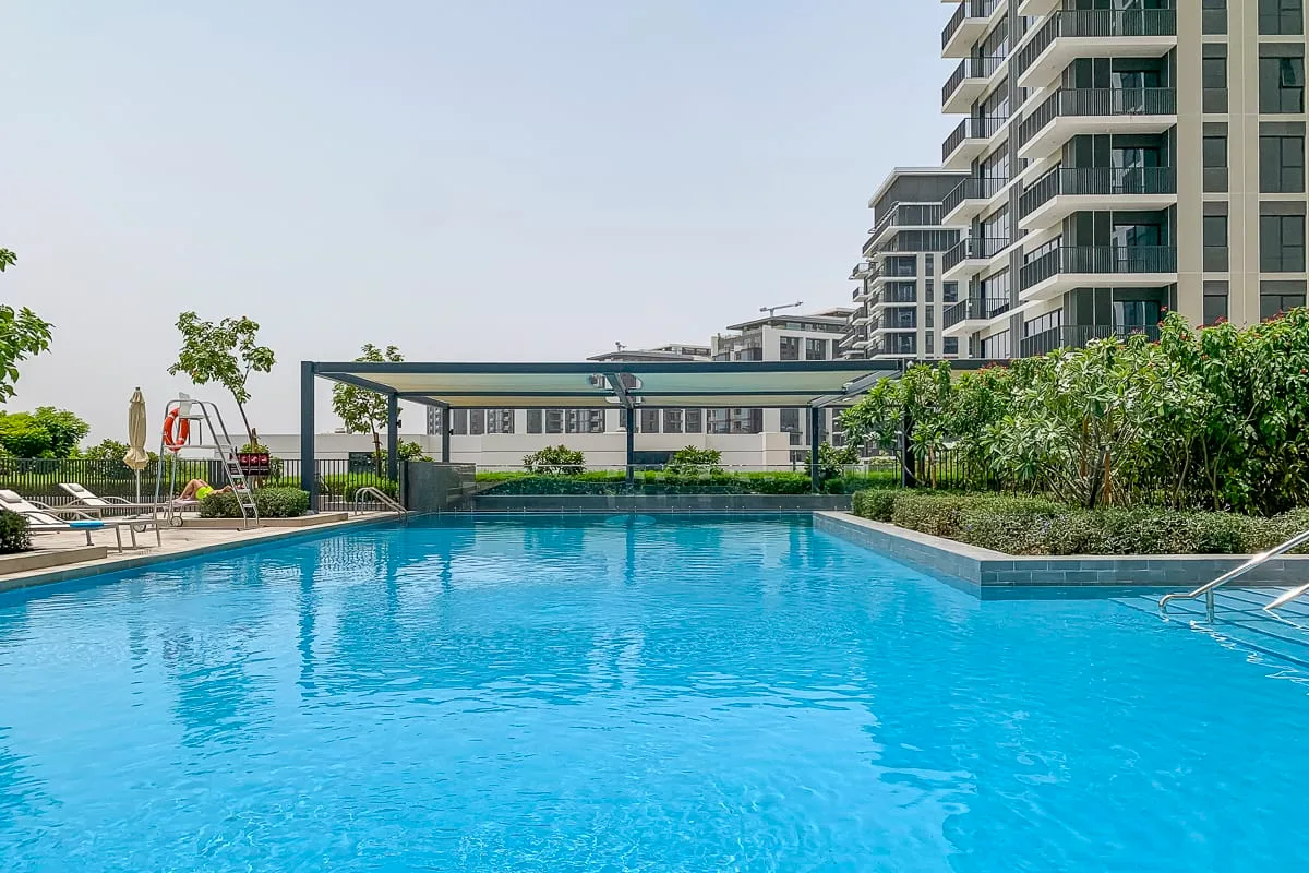 Una piscina al aire libre junto a un edificio de apartamentos moderno y jardines.