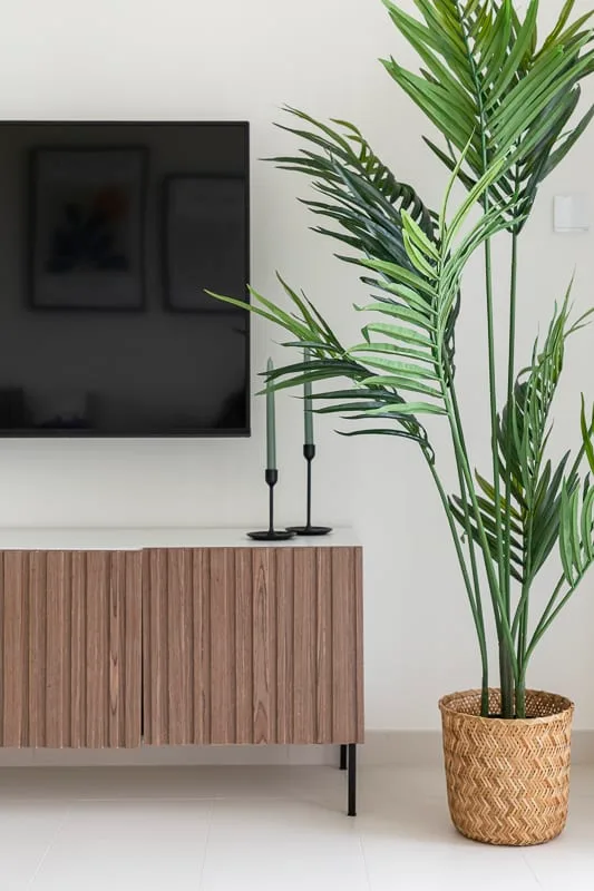 A living room with a television above a wooden cabinet and a potted palm.