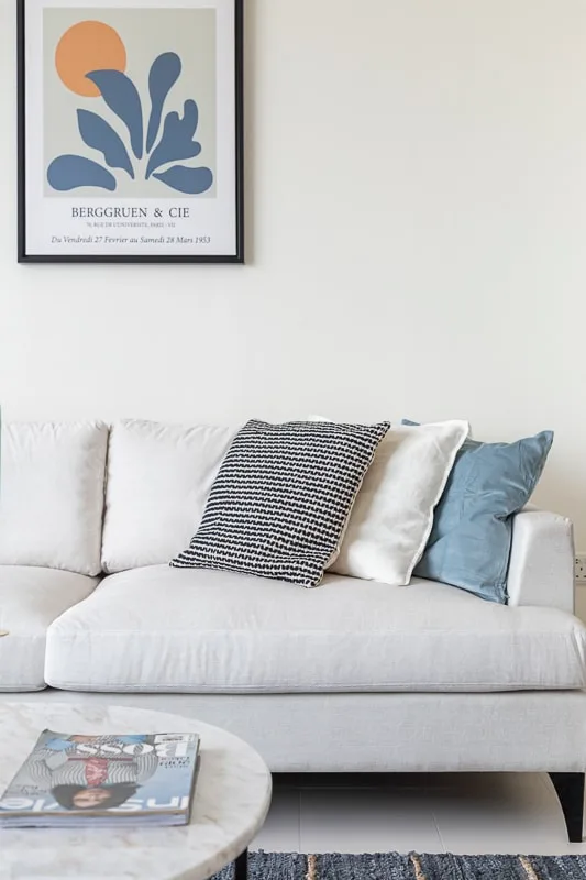 Una sala luminosa con un sofá blanco y una lámina botánica enmarcada.