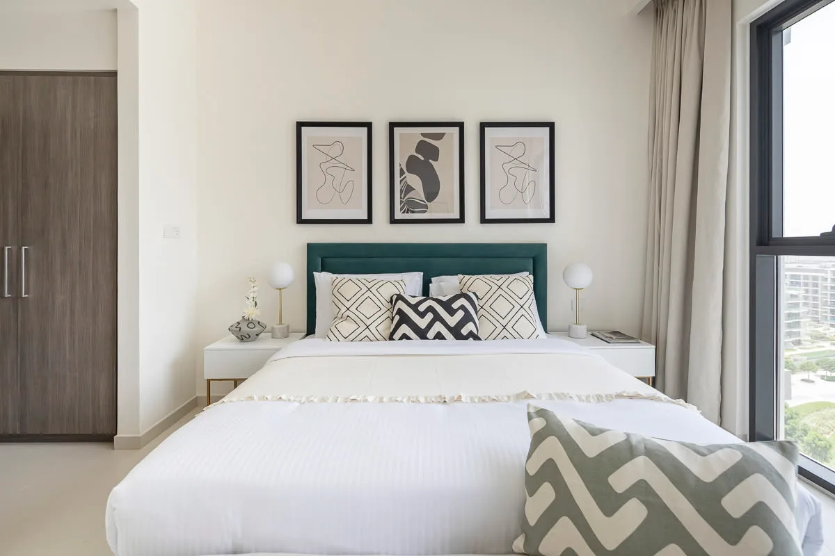 Un dormitorio luminoso con una cama bien tendida bajo tres láminas enmarcadas.
