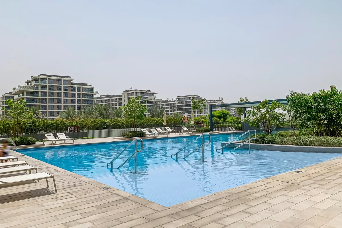 Una piscina al aire libre con pasamanos metálicos, rodeada por una terraza pavimentada.