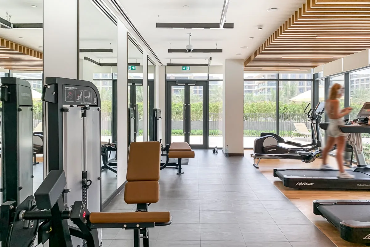 Un gimnasio luminoso con máquinas de ejercicio y cintas de correr junto a ventanales.