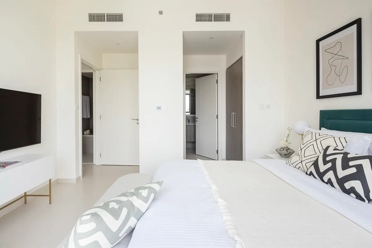 Un dormitorio luminoso con una cama grande, un televisor en la pared y una obra enmarcada.