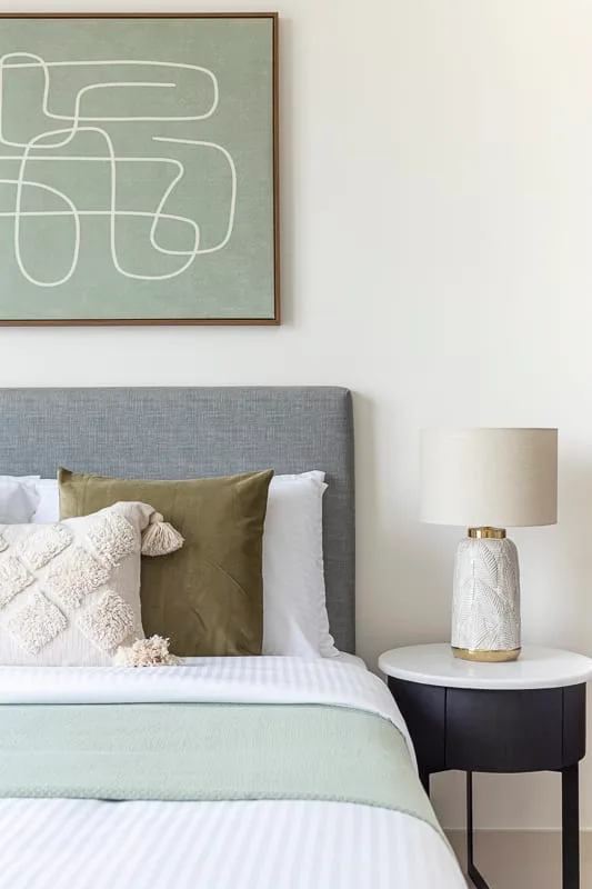 Una cama bien tendida con varias almohadas está bajo una obra abstracta enmarcada.