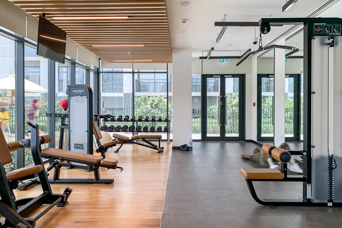 Una sala de fitness con máquinas de ejercicio, bancos y grandes ventanales.