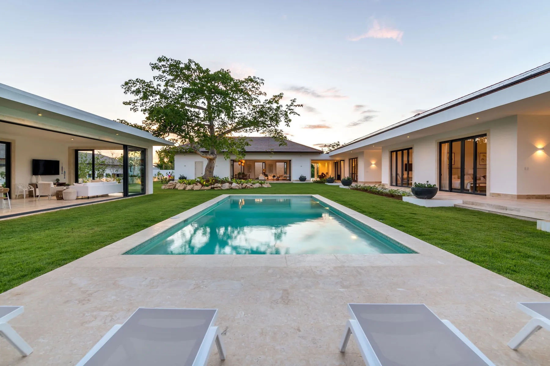 Una casa moderna rodea una piscina y un patio ajardinado.