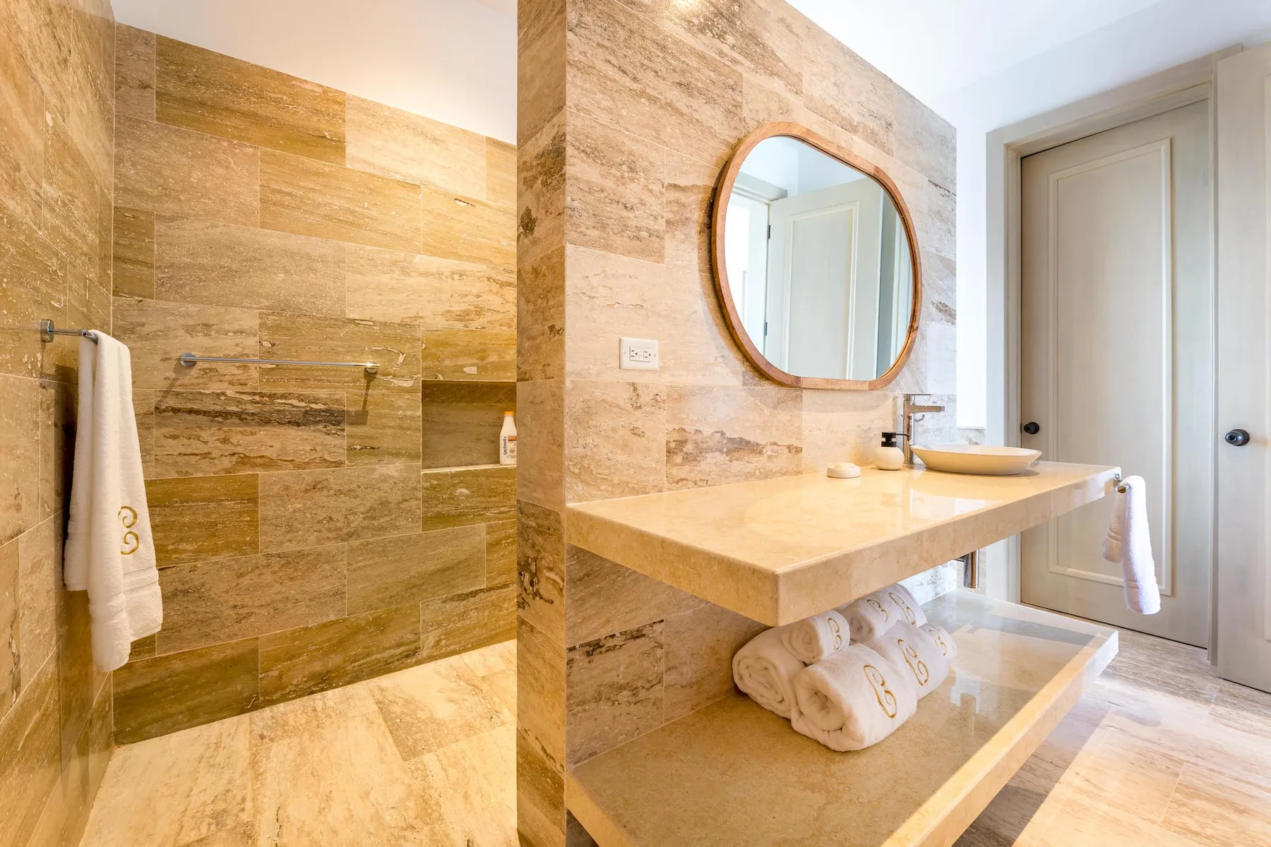 A bathroom with a stone shower area and a vanity beneath a round mirror.