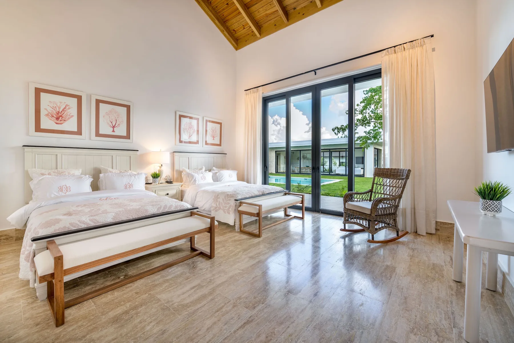 A bright bedroom with two beds and a glass door opening onto a garden.