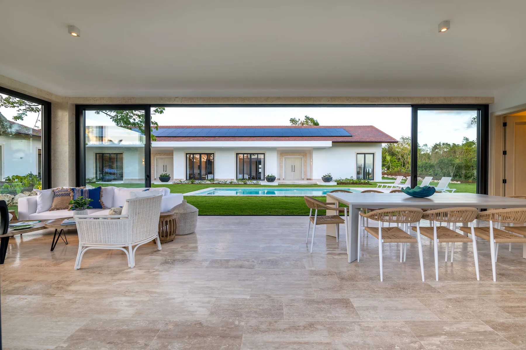 An open indoor dining and seating area overlooks a lawn and a modern house.