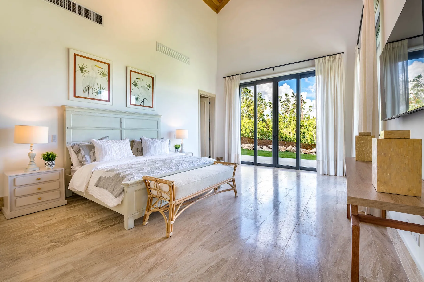 A bright bedroom with a large bed and glass doors opening onto a garden.