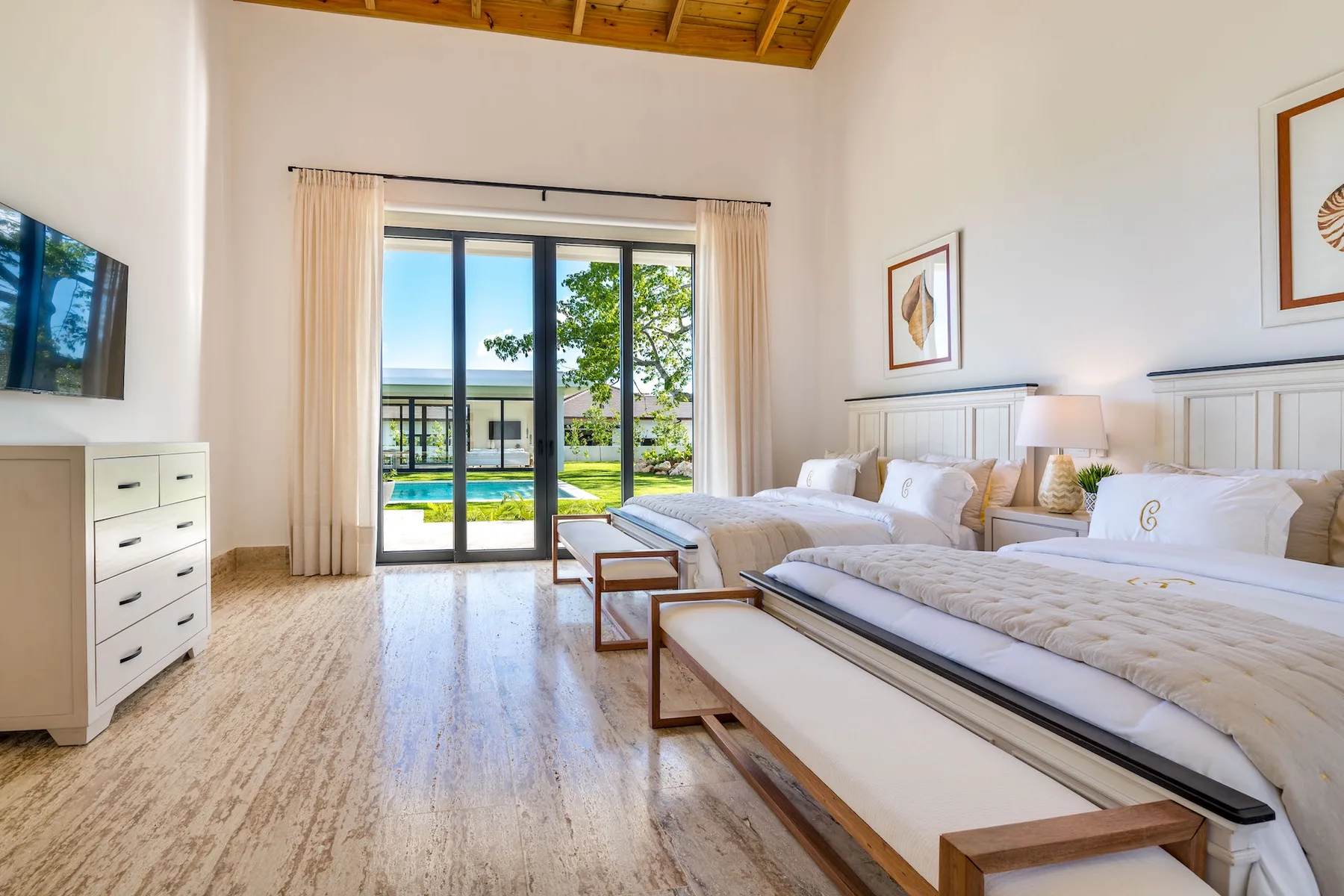 A bright bedroom with two beds and glass doors opening onto a garden.