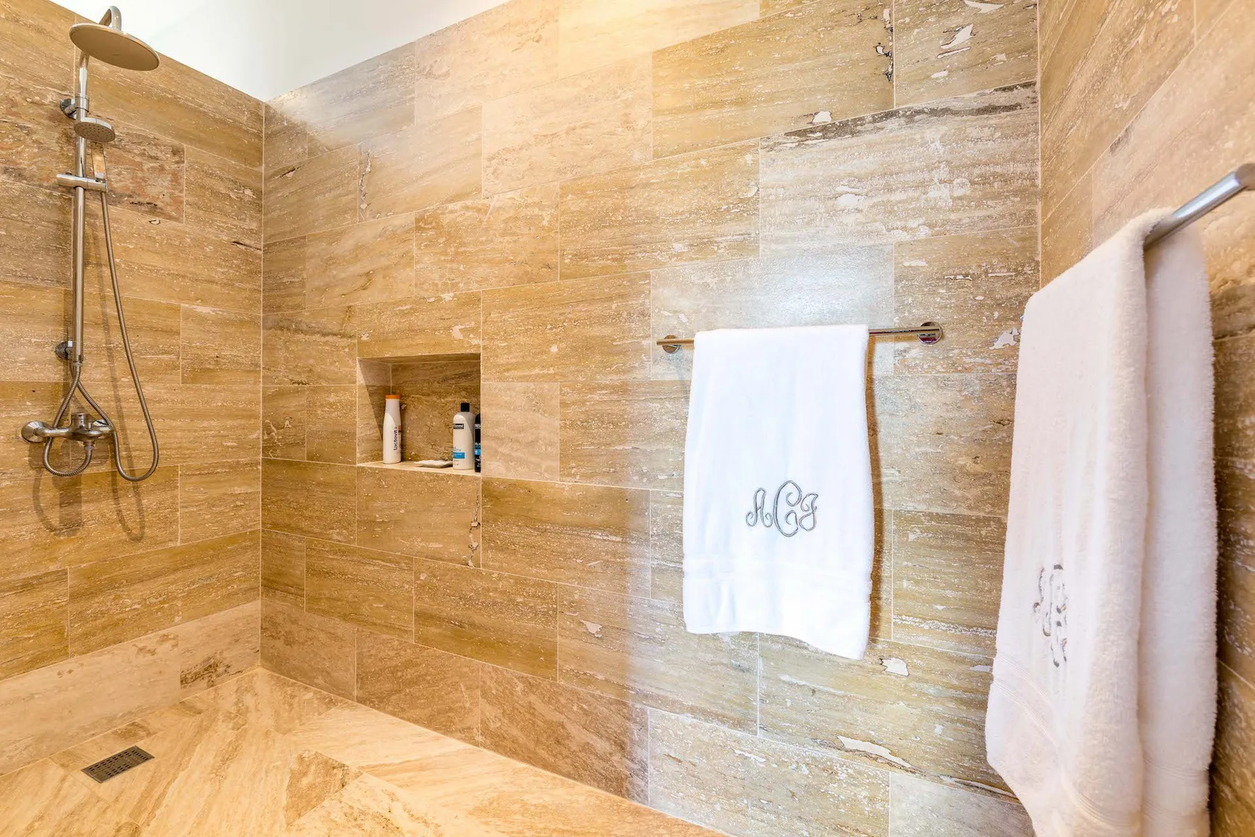 A tiled bathroom with a wall-mounted shower and white towels.
