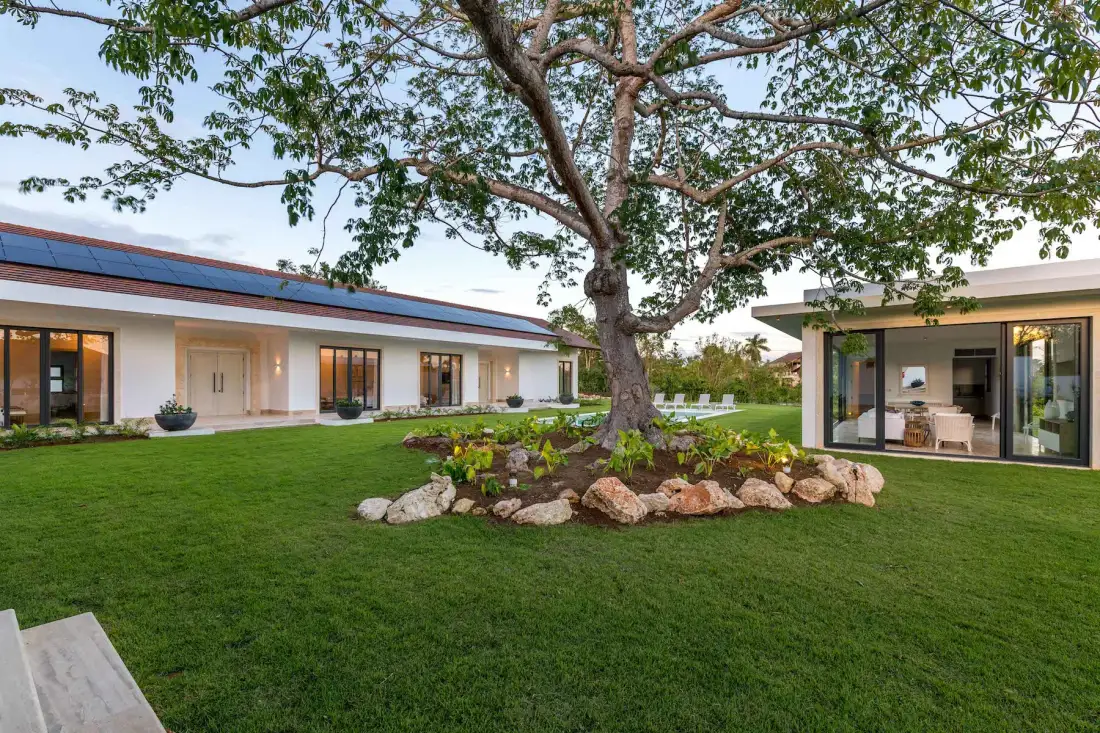 A modern home surrounds a landscaped lawn with a large tree and glass-fronted living area.