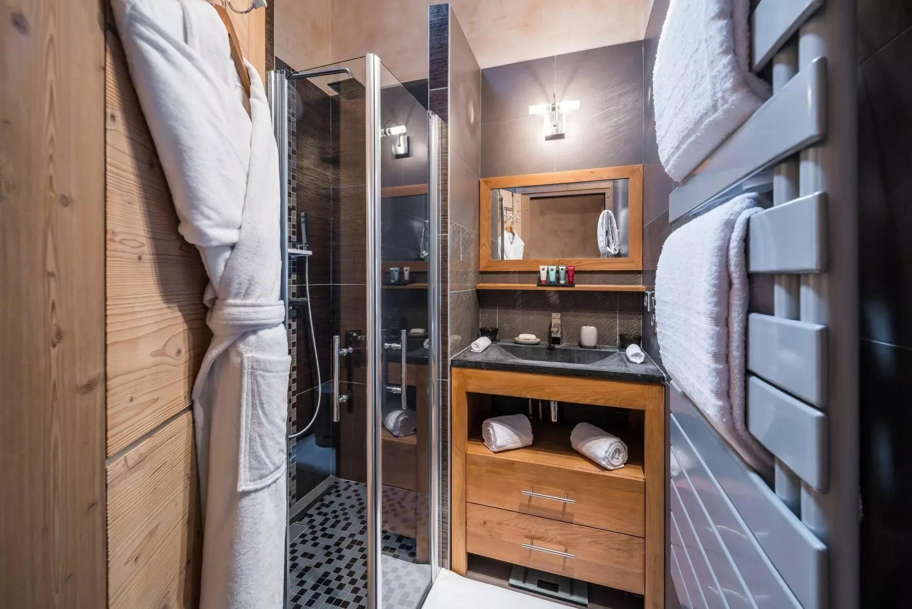 A bathroom with a glass shower, wooden vanity, and wall-mounted towel warmer.